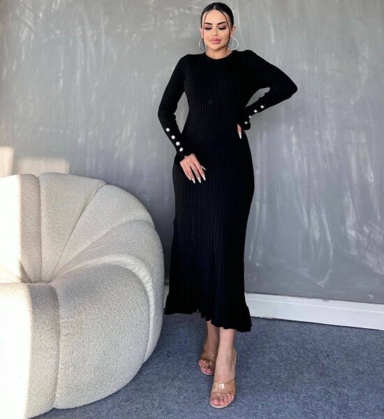 A woman wearing a black dress with long sleeves and heels.