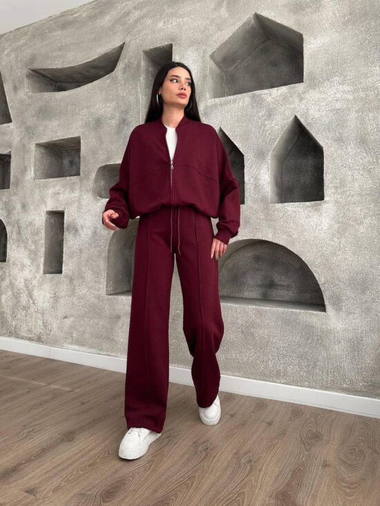 A Zae woman in a burgundy casual set standing in front of a wall.