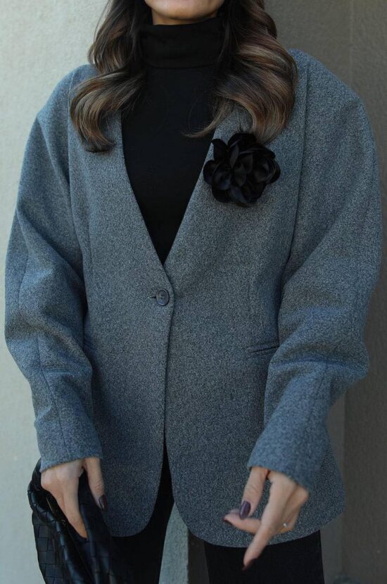 A woman wearing a S.Yalda grey blazer with a flower on it.